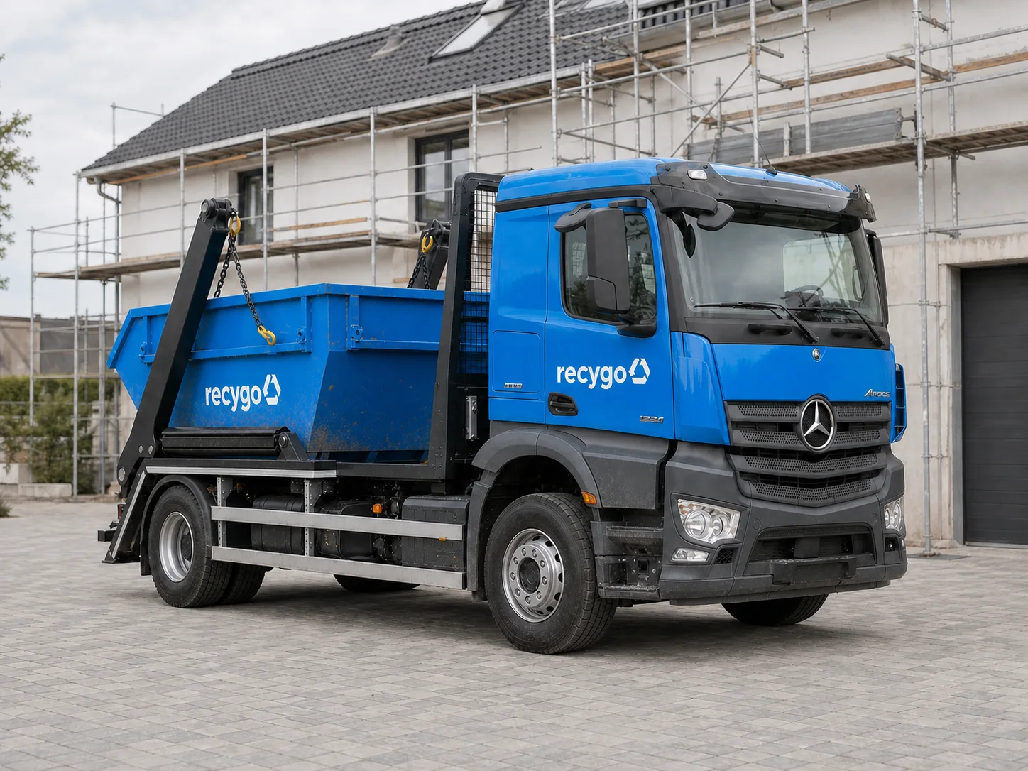 Kék Recygo konténerszállító teherautó egy felújítási helyszínen